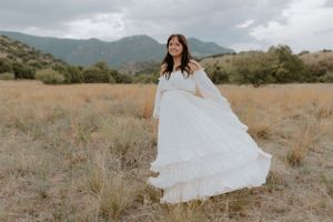A billowing white dress stands out against golden grasses and mountain scenery.
