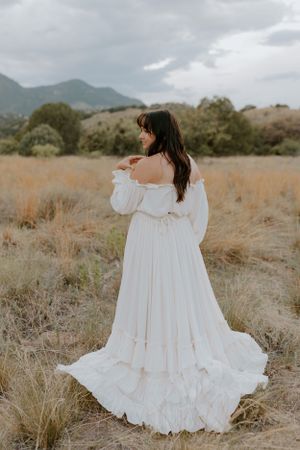 A romantic white dress with flowing sleeves photographed in a mountain meadow setting.
