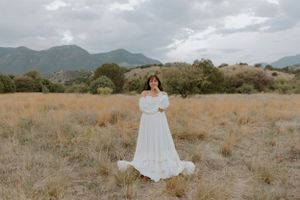 An elegant white dress stands still in a desert field with mountains in the background.