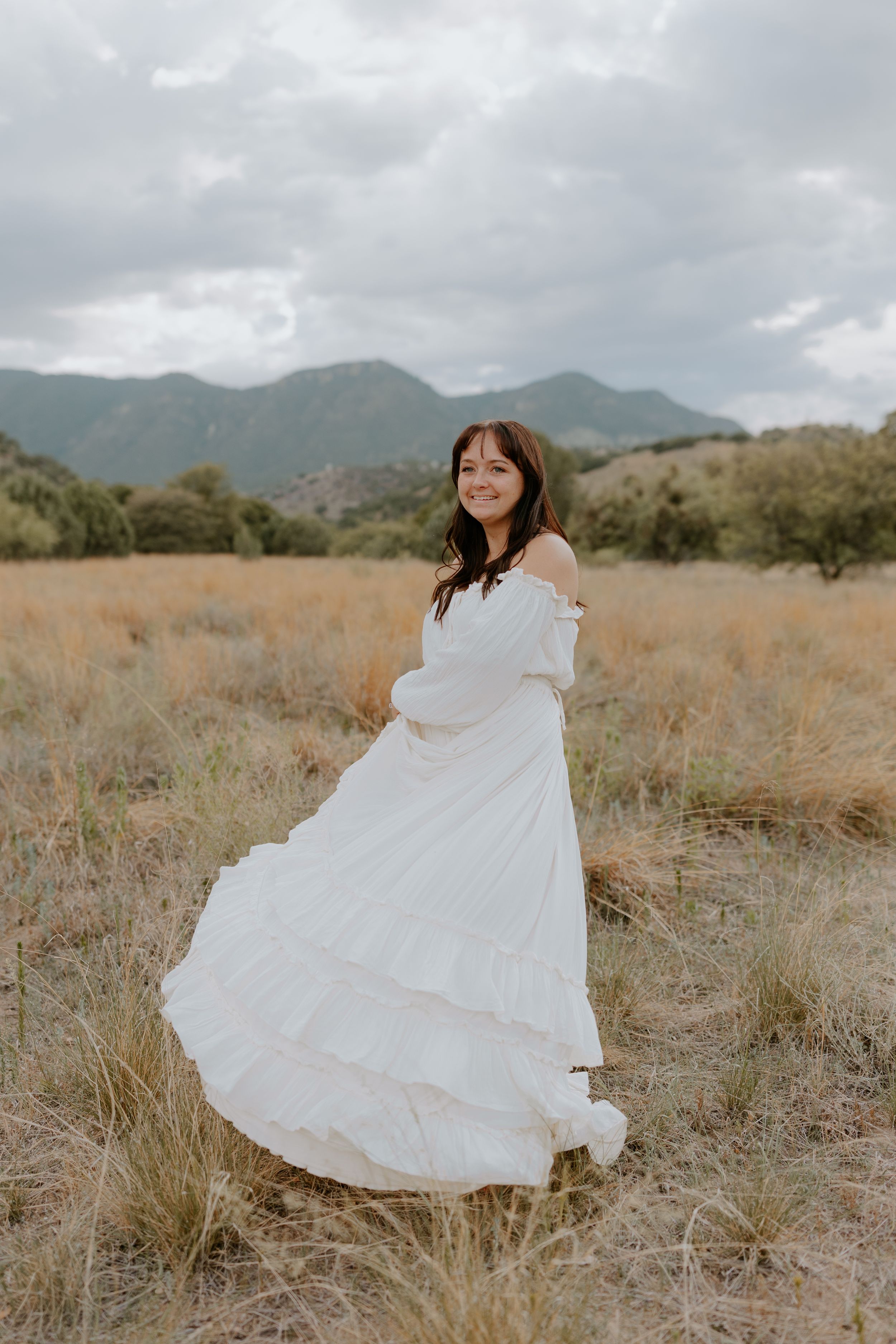 An ethereal white gown flows in the wind against mountains and dry grassland.