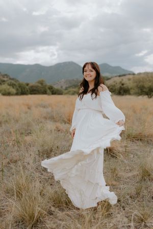 A flowing white dress moves gracefully in the wind against a mountainous landscape.