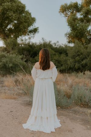 Back view of white ruffled dress against desert brush and trees.
