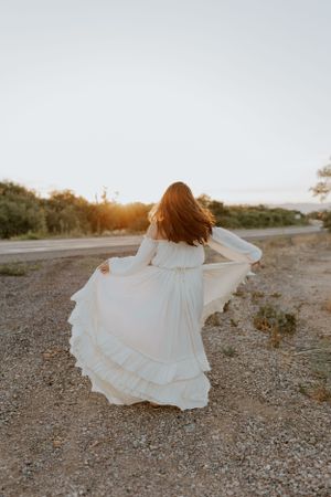 Woman in white dress spinning gracefully on desert path at golden hour.