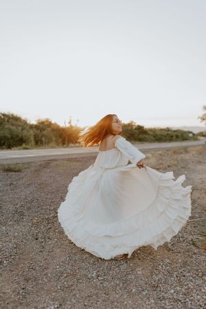 White ruffled dress spins dramatically on a dirt path during sunset.