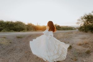 Long white dress flows elegantly across a desert path at sunset.