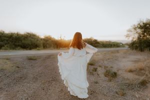 Flowing white dress catches the light while spinning on a desert trail.