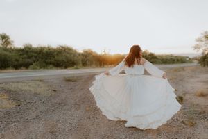 Elegant white dress dances in motion against desert brush at sunset.