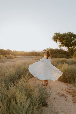 White dress twirls among desert sage brush during golden hour.