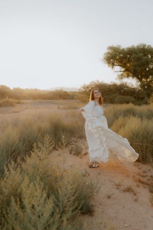 Dreamy white gown flows through desert landscape at sunset.