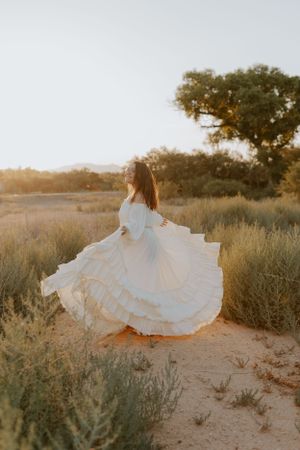 A flowing white dress twirls gracefully against a desert landscape with sage brush and trees at sunset.