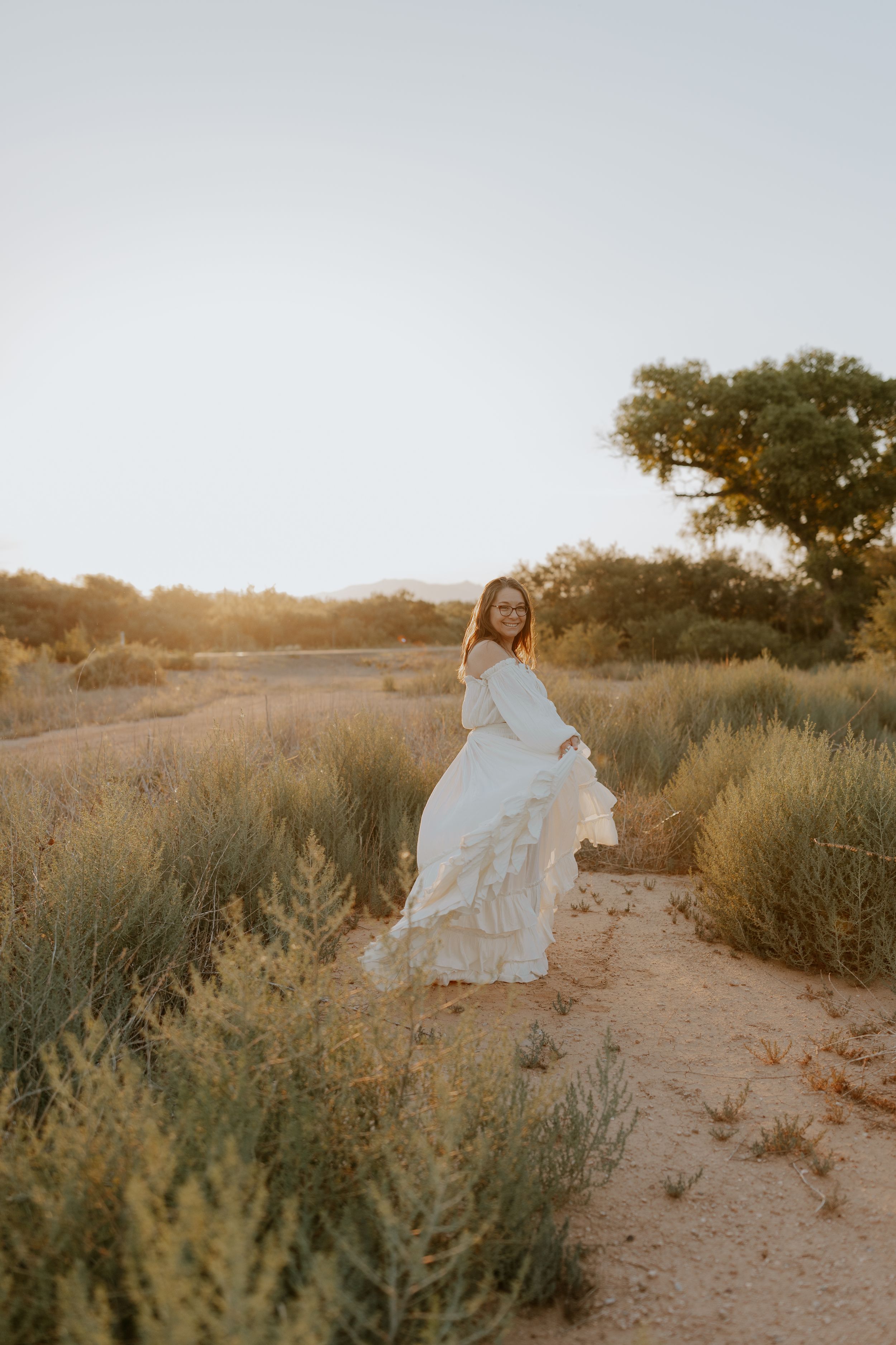 A flowing white dress moves through desert brush and trees at golden hour.