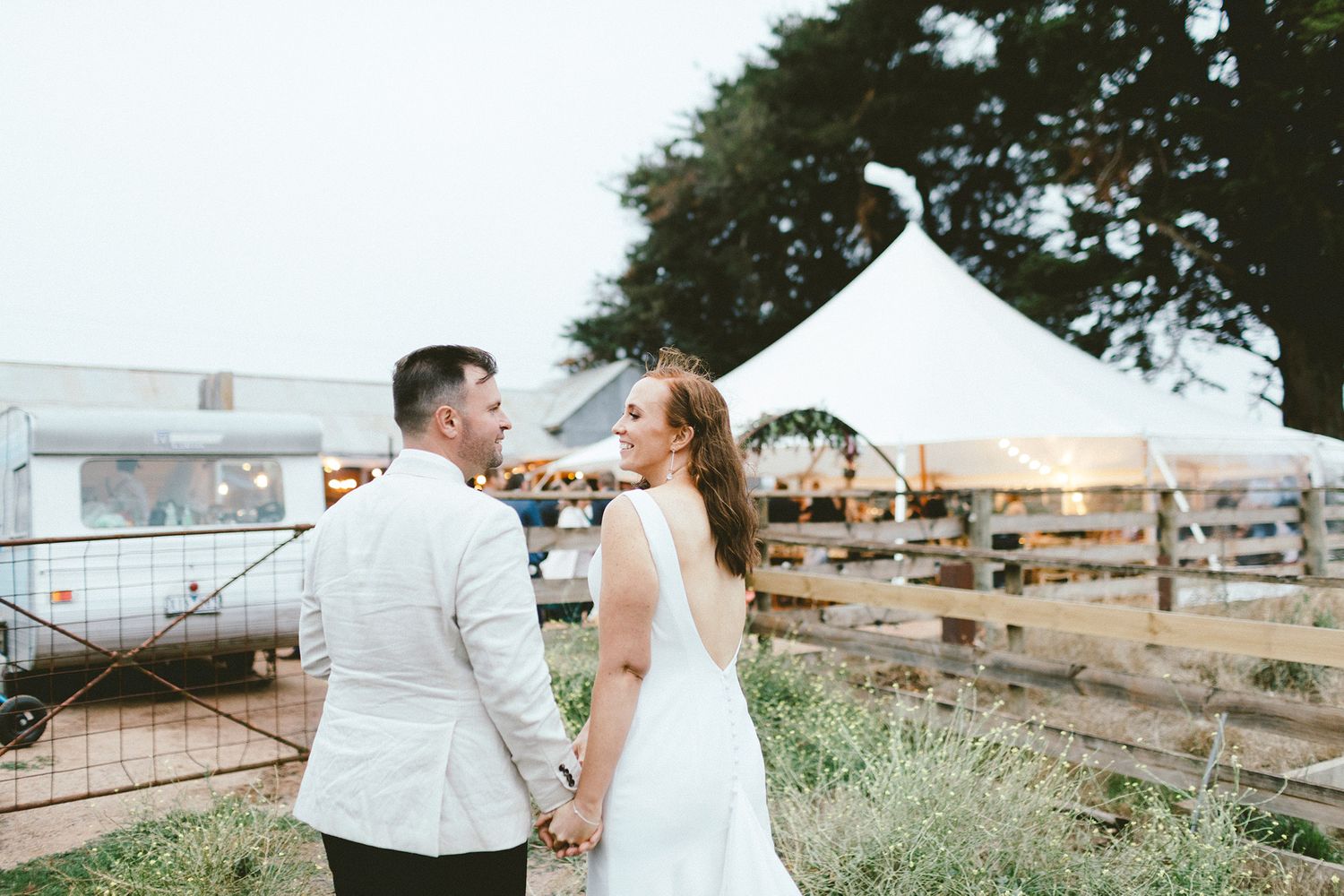 Wedding couple sharing intimate moment by fence with white tent in background.