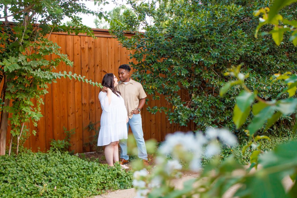 A couple poses together in a lush garden setting with a wooden fence behind them.