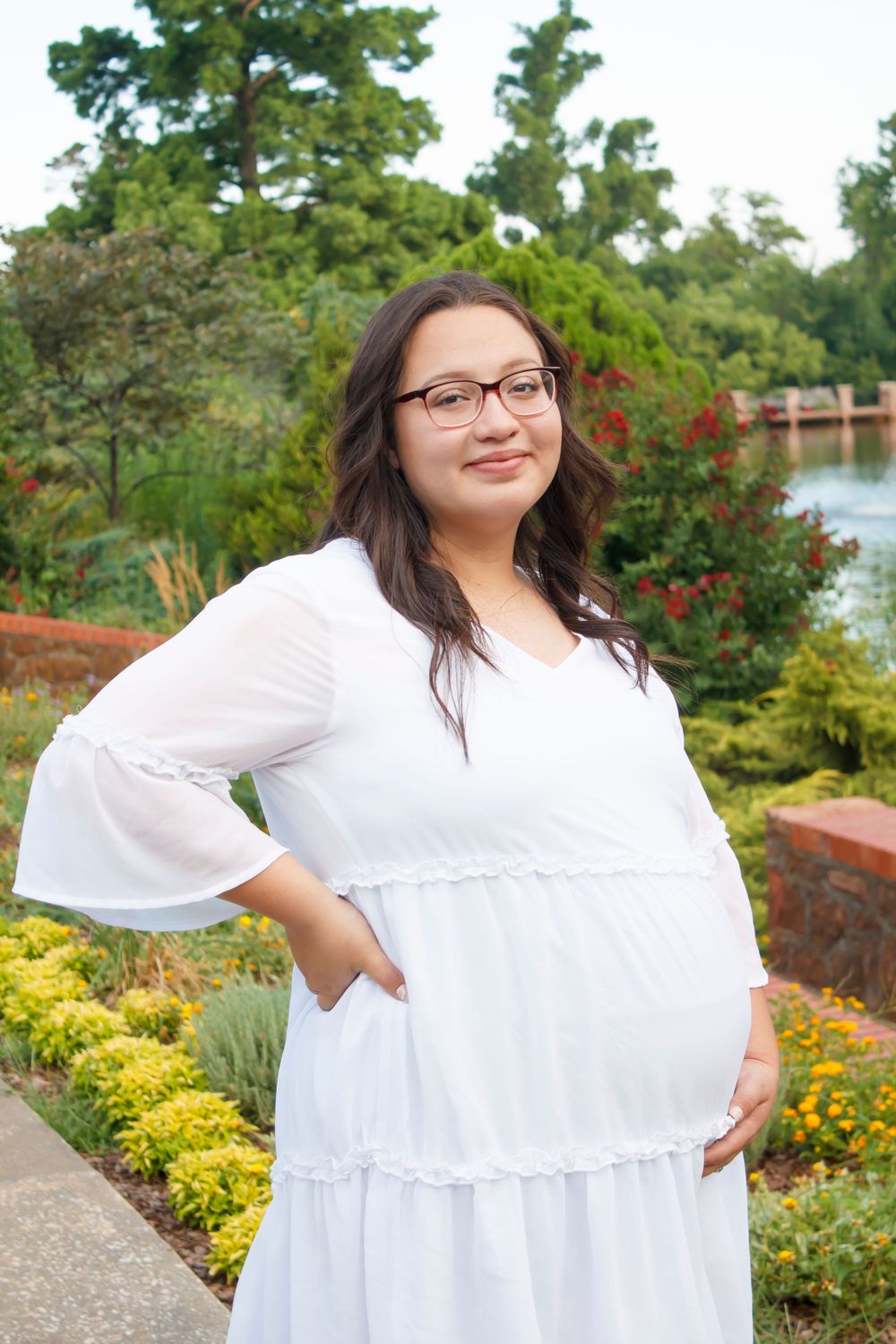 A maternity photo taken in a garden setting with colorful flowers and a lake in the background.