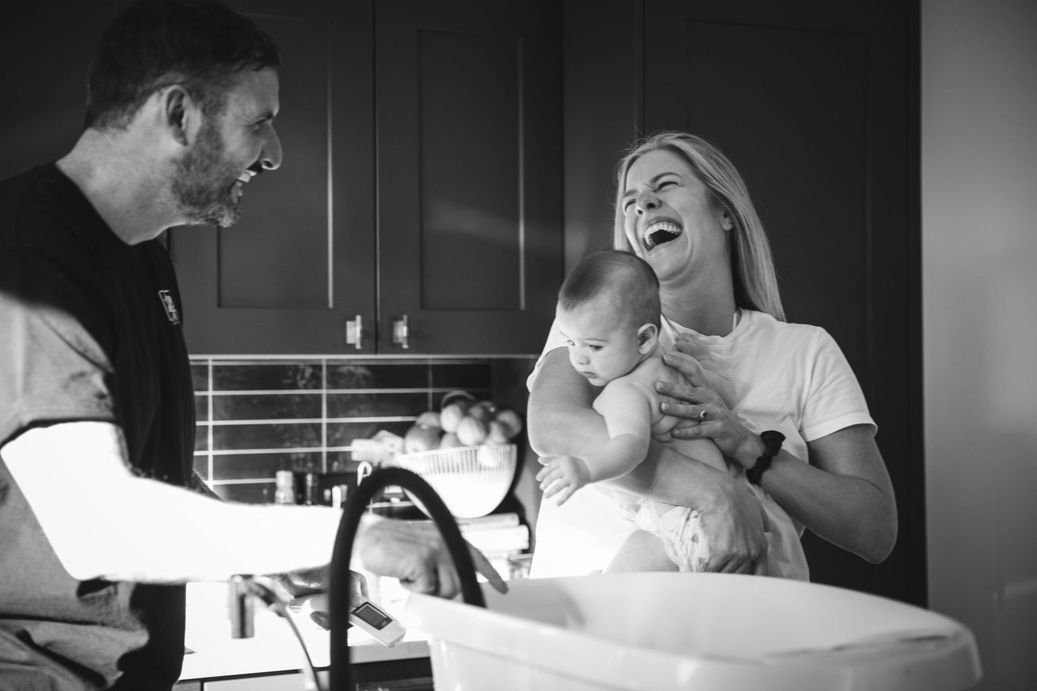 Black and white candid kitchen scene shows laughter and joy during bath time.