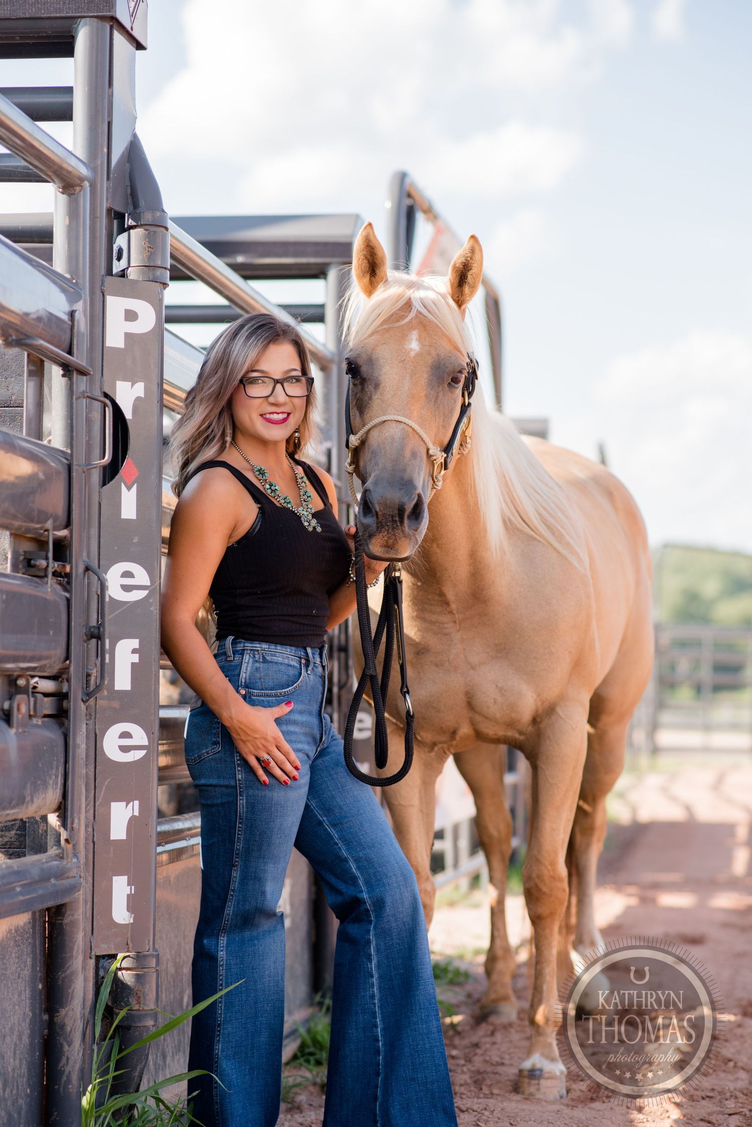 A gentle palomino horse stands next to someone in denim and black top by metal horse stalls.