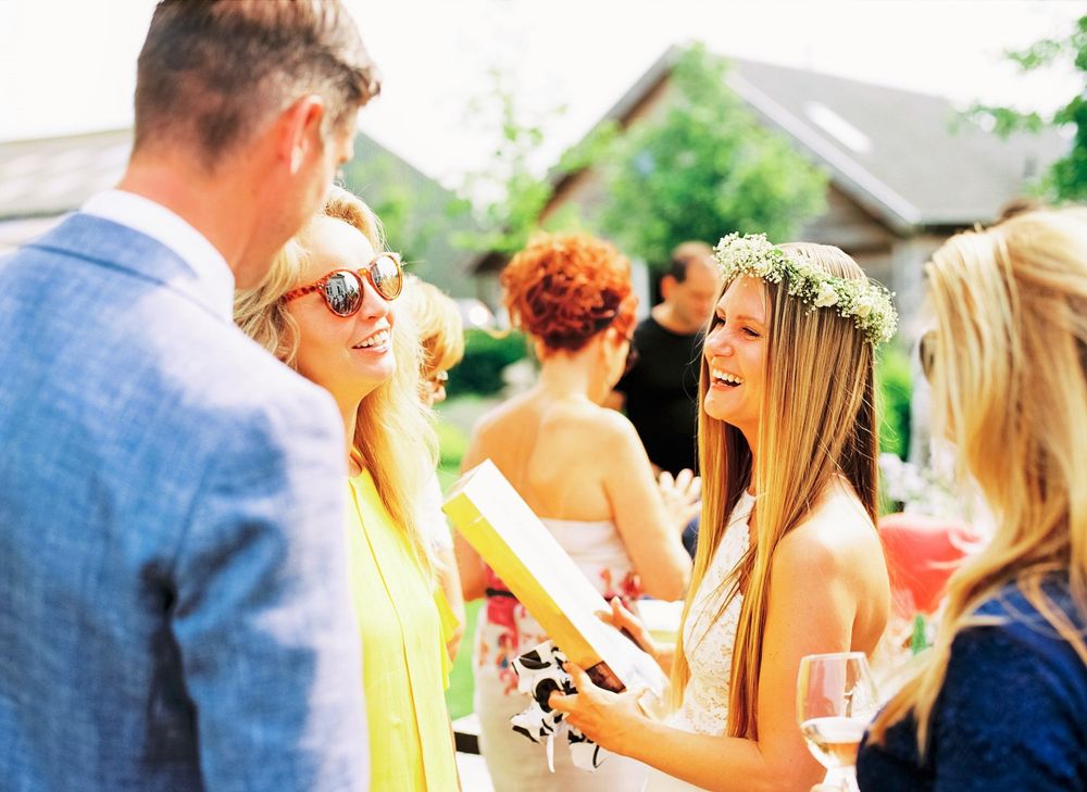 A group of wedding guests in summer attire gather outdoors for conversation and drinks.