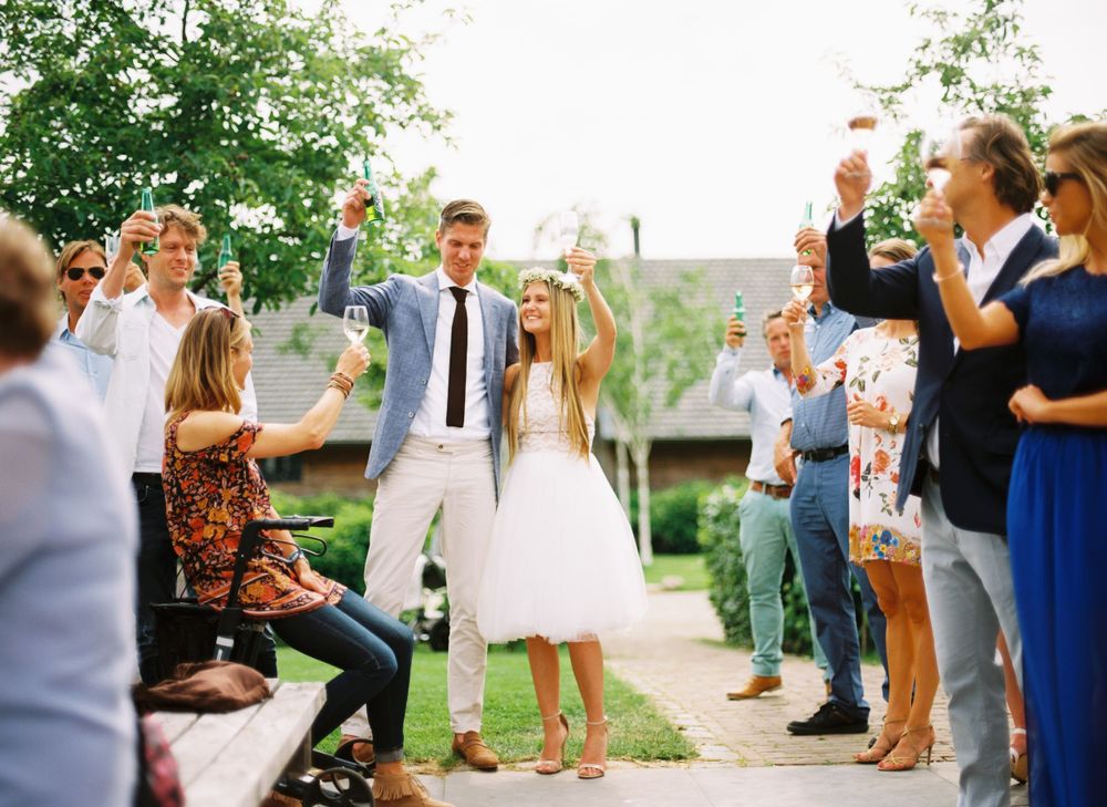 Wedding guests celebrate and toast around a couple at an outdoor garden reception.