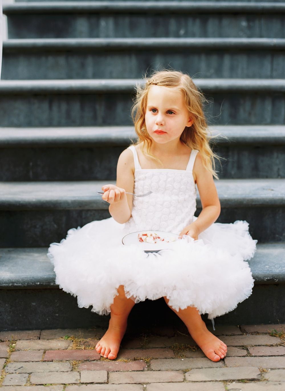 A child in a white tutu dress sits barefoot on concrete steps.
