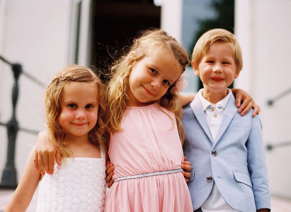 Three children in formal attire pose together on outdoor steps.