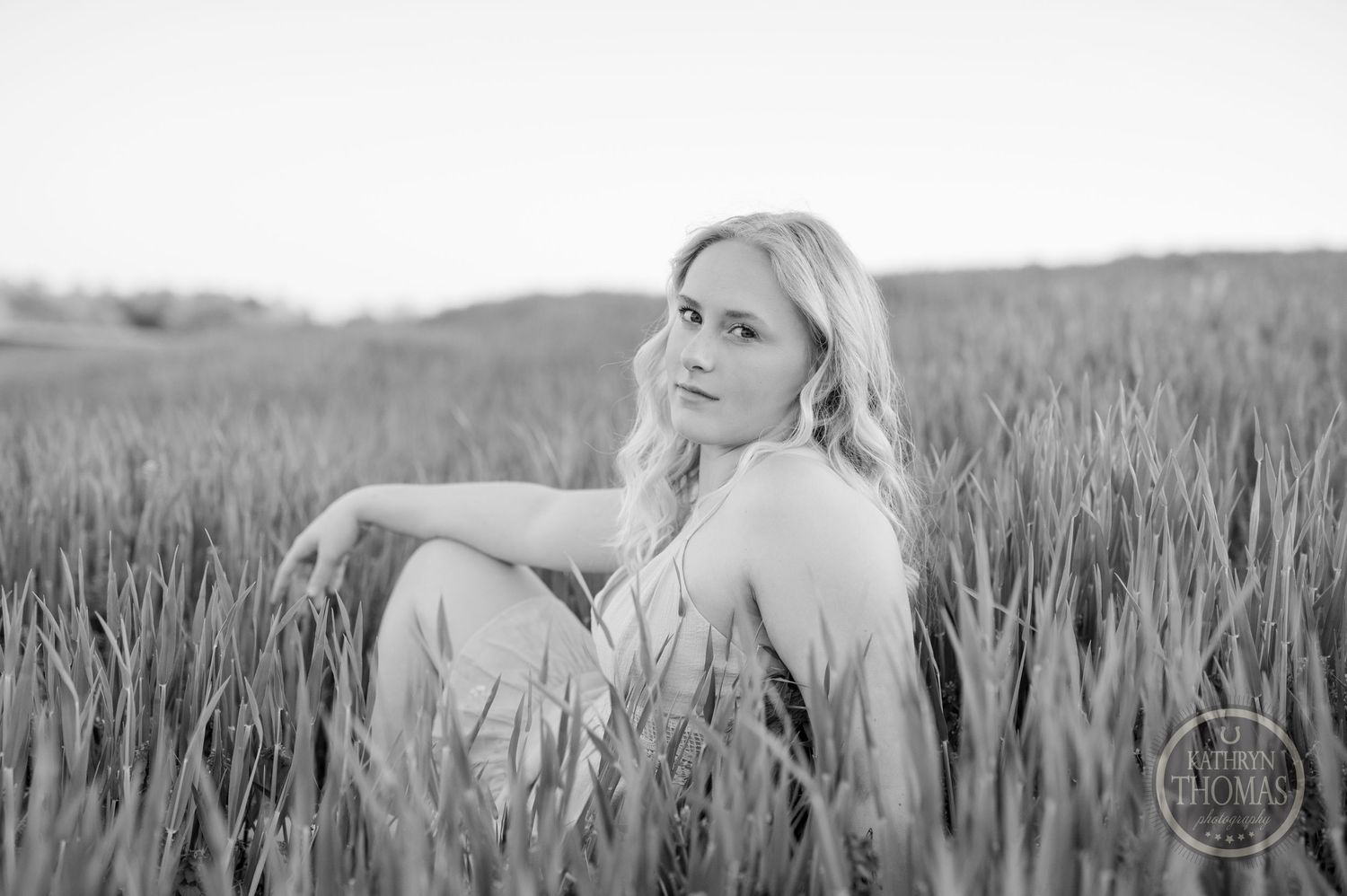 Black and white portrait of figure sitting peacefully in tall grass field.