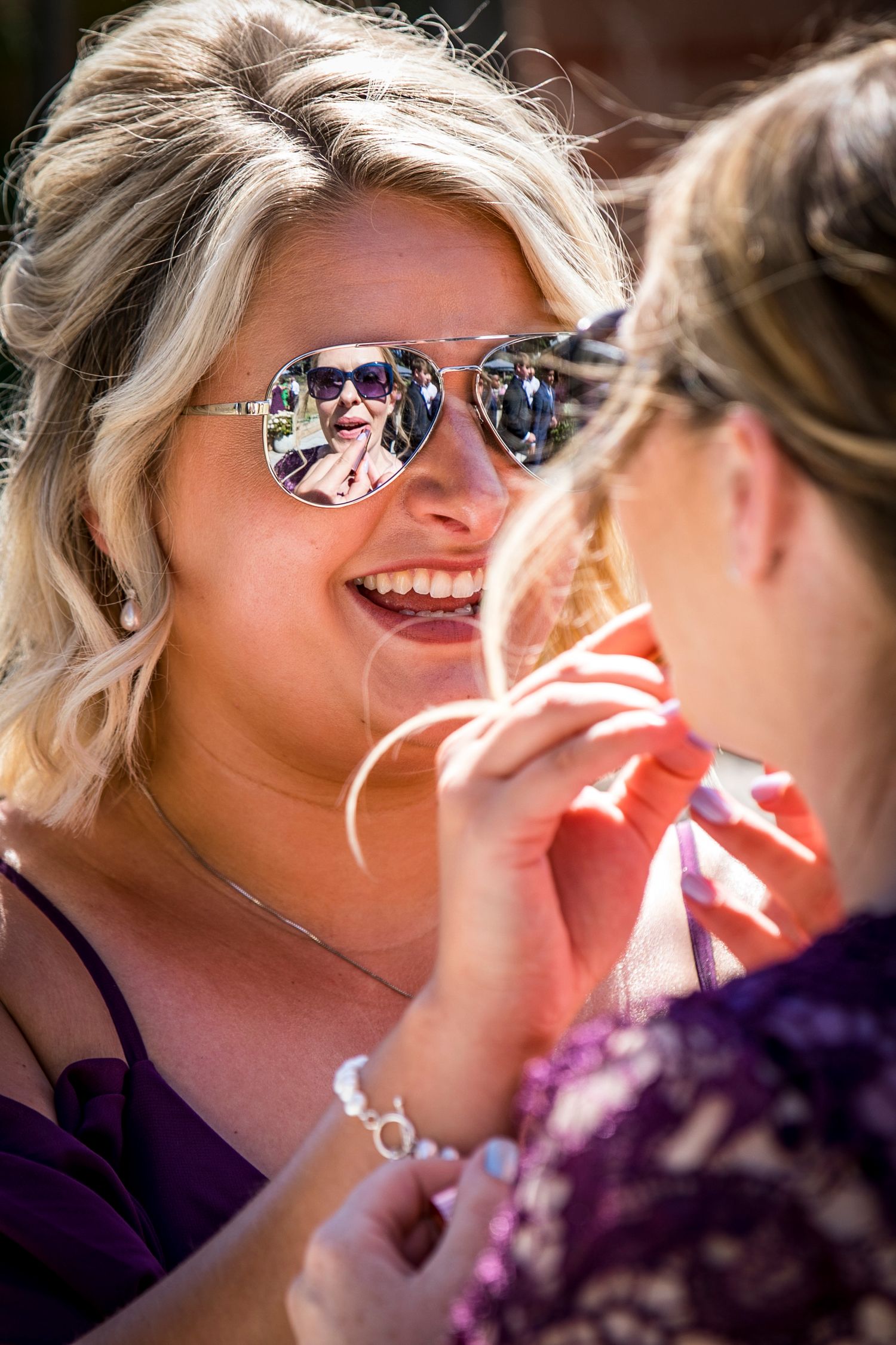 Close-up of sunglasses reflecting a sunny outdoor wedding scene.