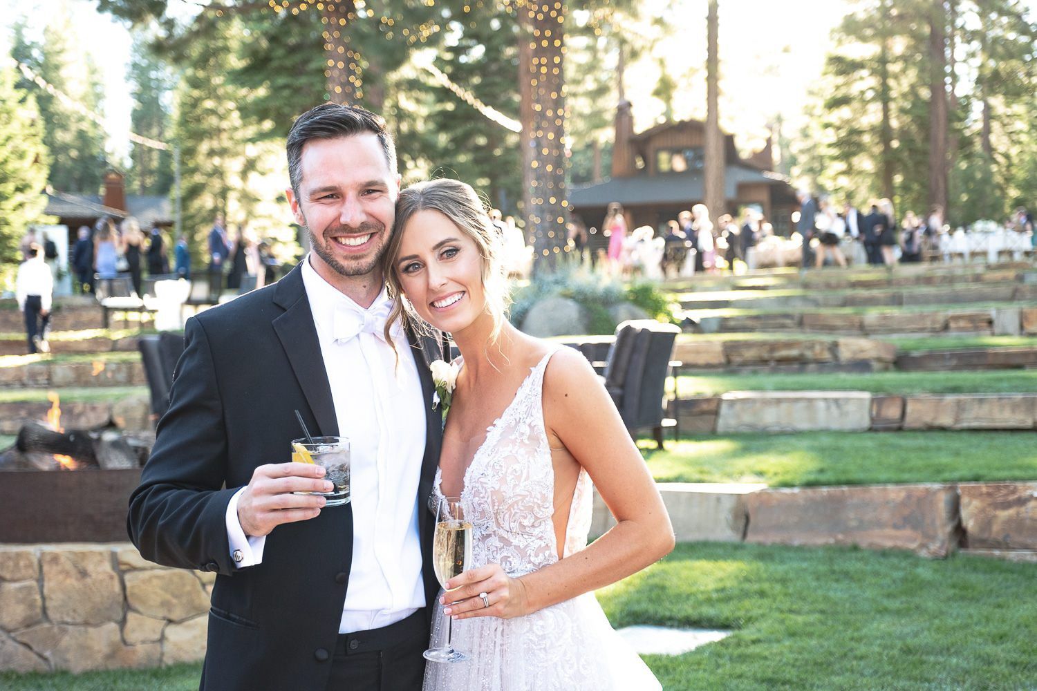 A happy couple celebrates their wedding day outdoors at a rustic mountain venue with tall pine trees in the background.