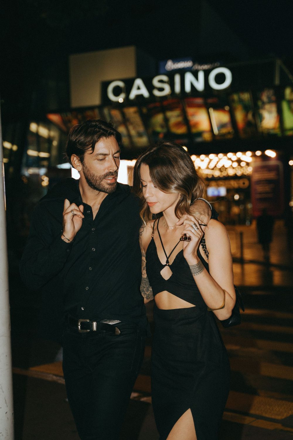 Stylish couple in black outfits dancing near illuminated casino at night.