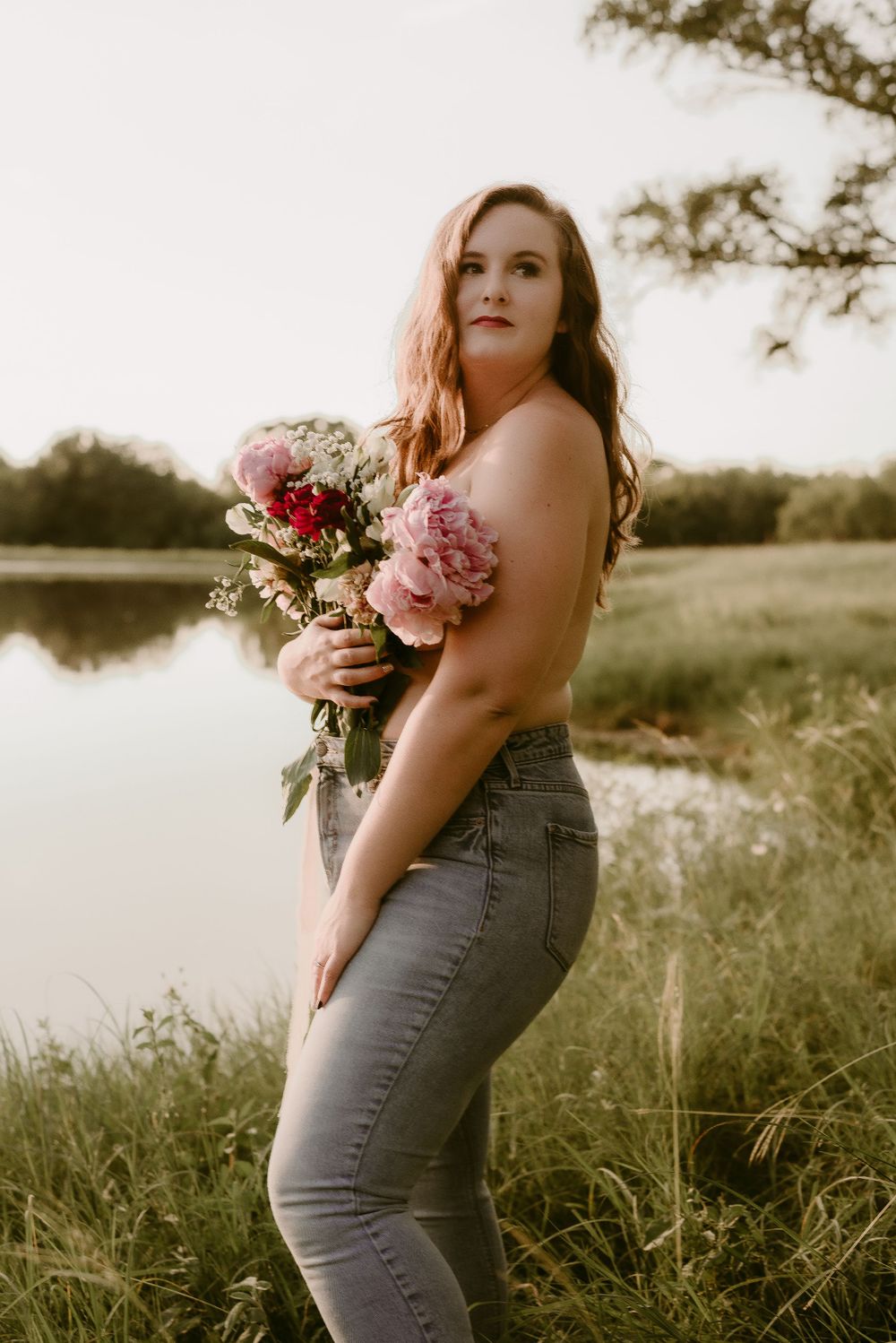 Intimate portrait with someone holding a bouquet of pink flowers beside a peaceful lake.