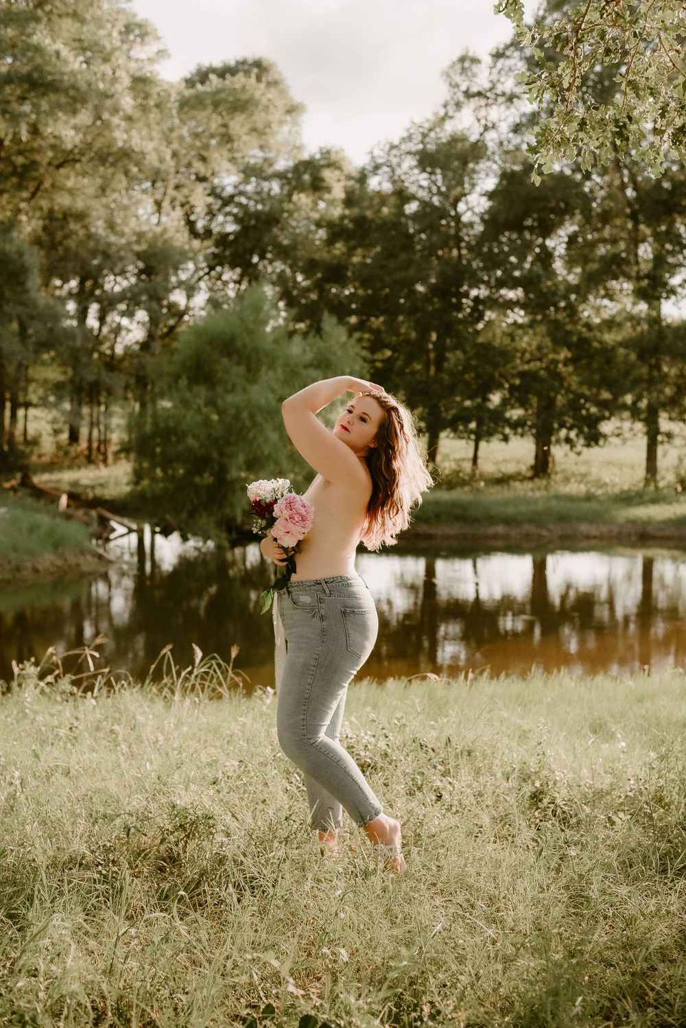 Artistic outdoor portrait with someone holding flowers beside a serene pond at golden hour.