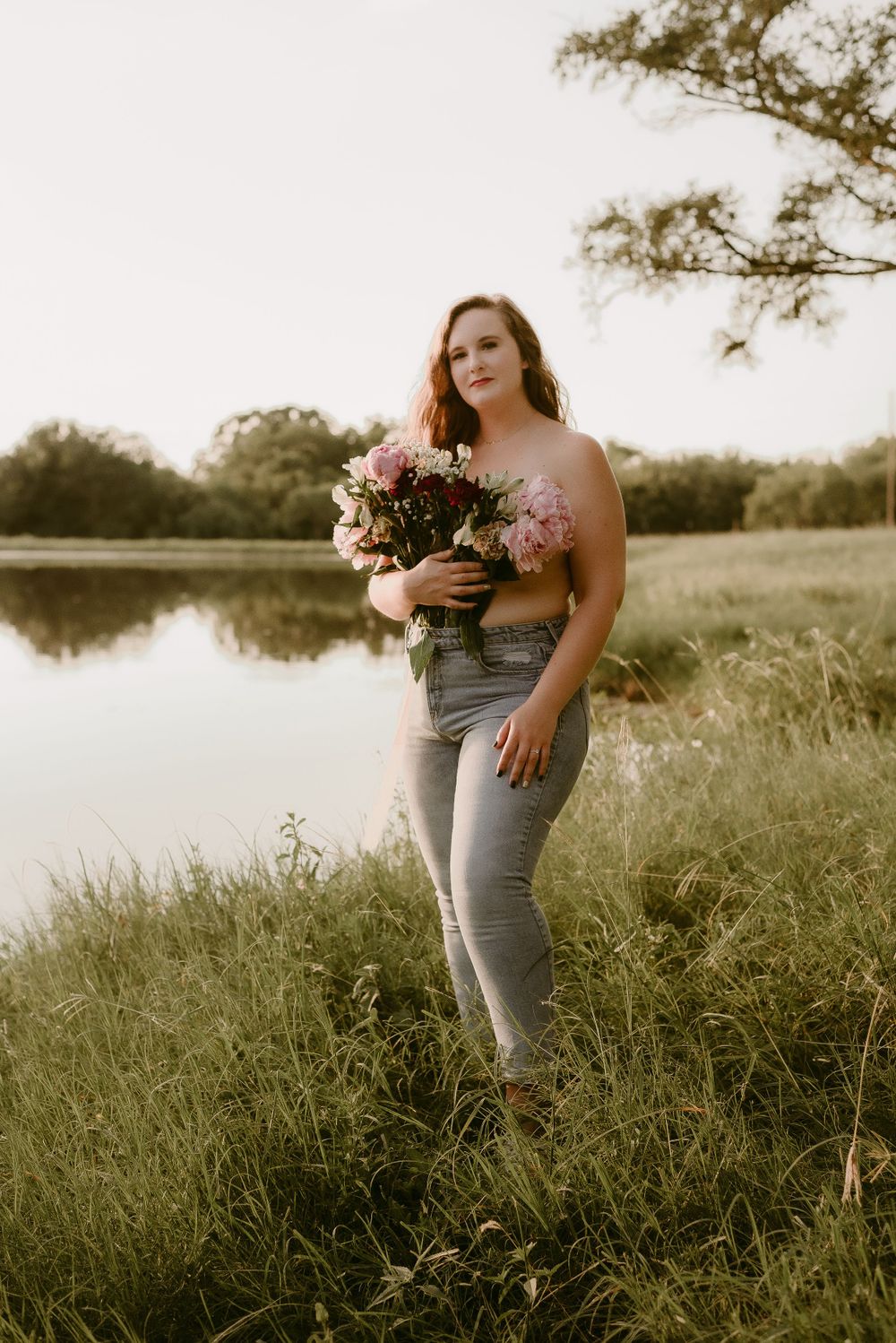 Natural outdoor portrait with someone holding pink flowers by a tranquil pond.