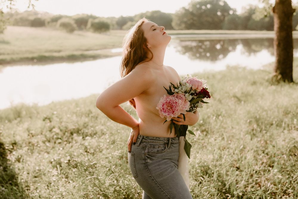 Sunset portrait by a pond with someone holding pink flowers and arching backwards.