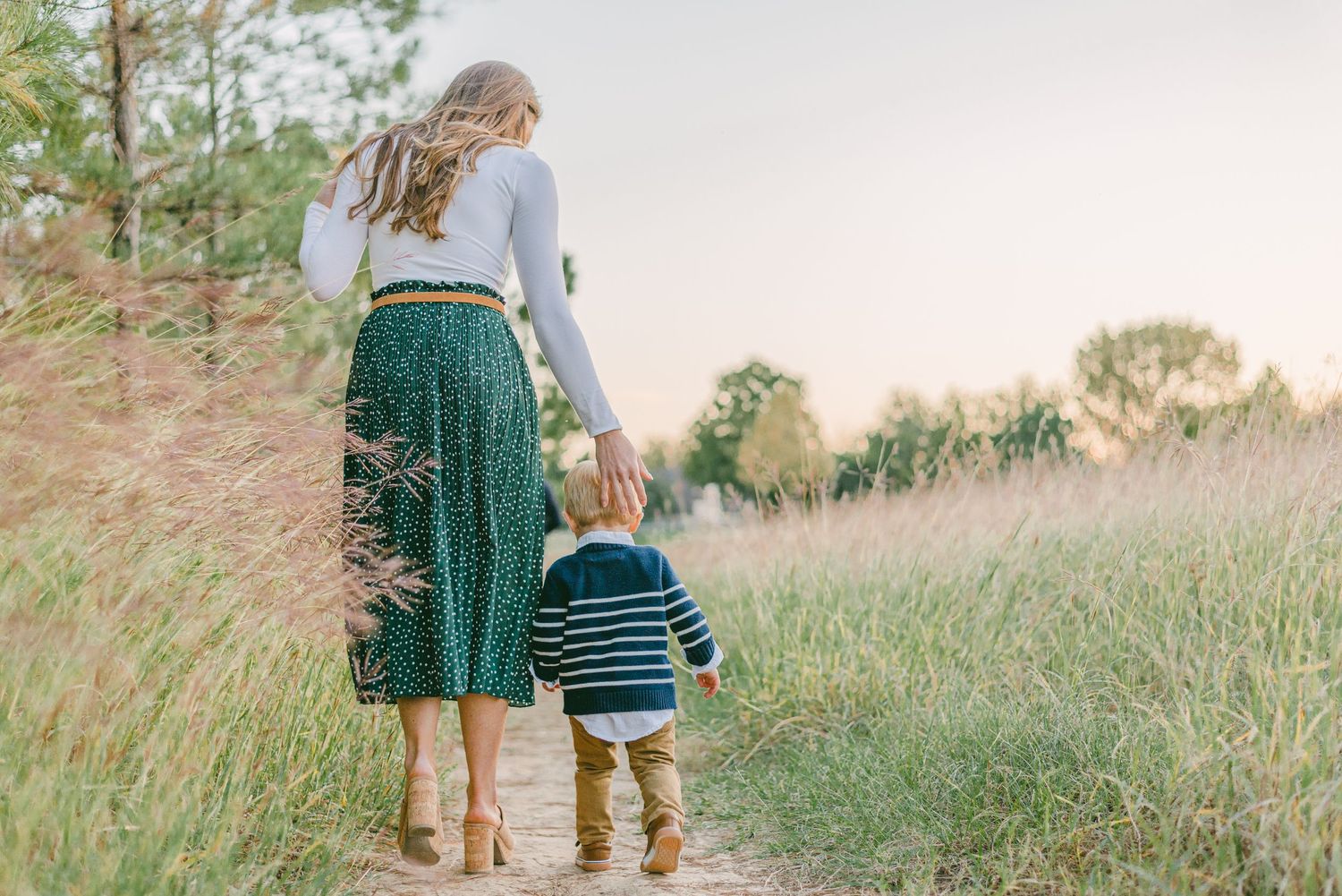 a mom gently guides her son along the trail in tall grass