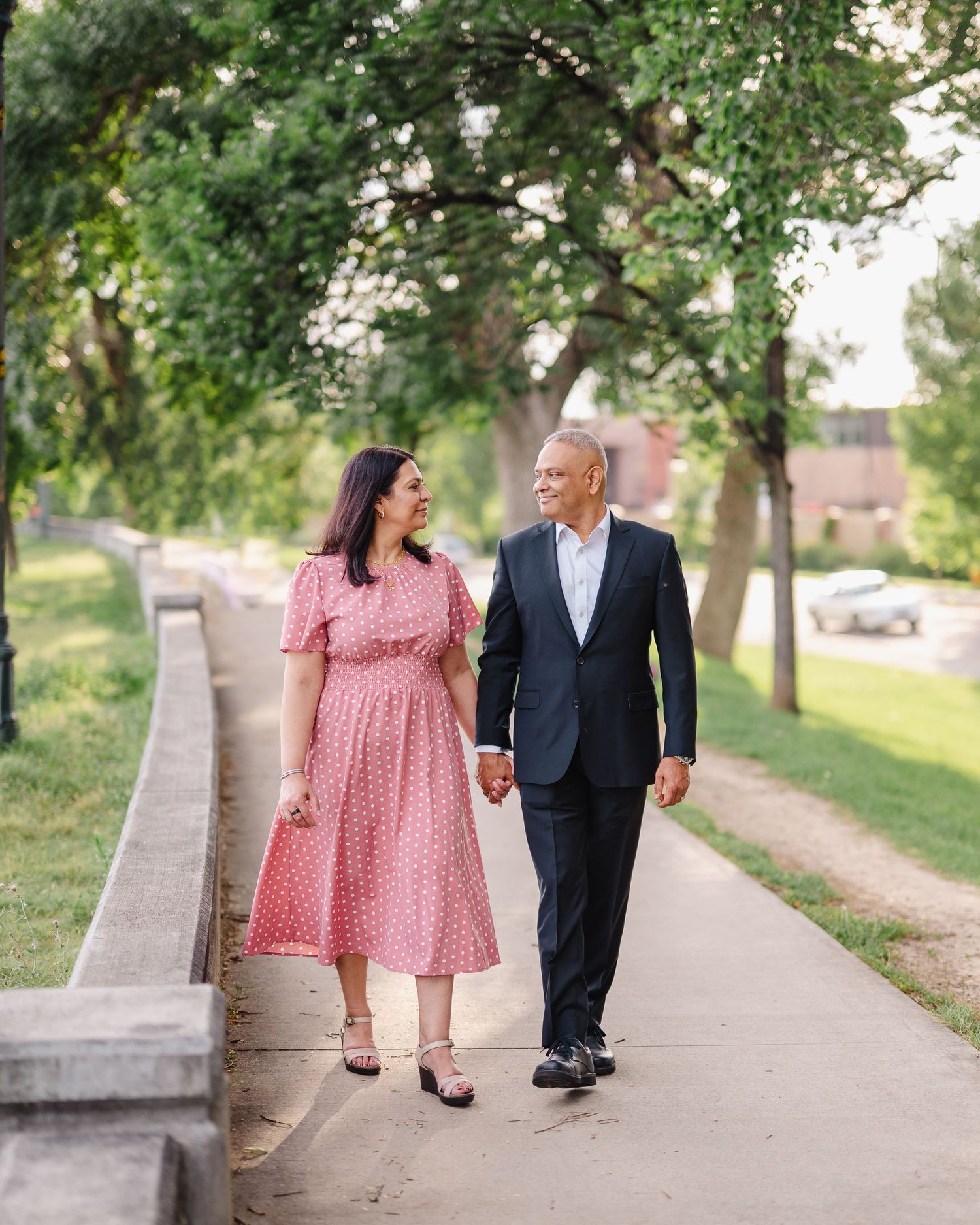 Couple taking a romantic stroll along a tree-lined pathway in casual attire.