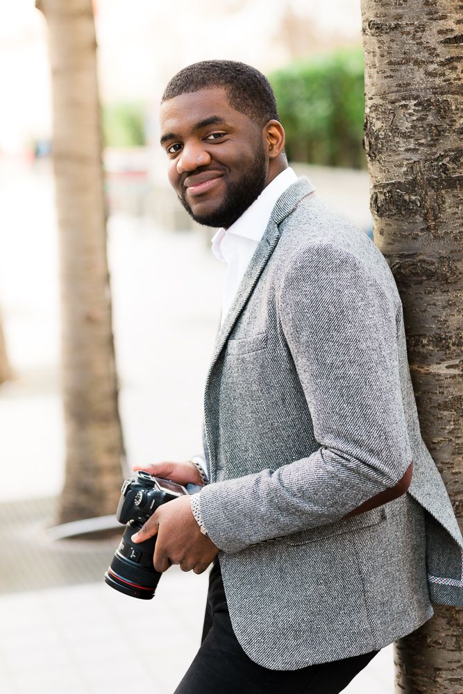 Portrait of photographer in grey blazer holding camera outdoors.