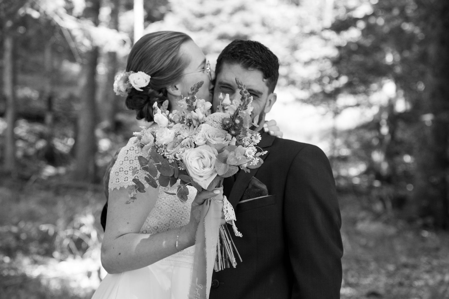 Photo en noir et blanc d'un couple en forêt. Le magnifique bouquet de la mariée cache leur visage.
