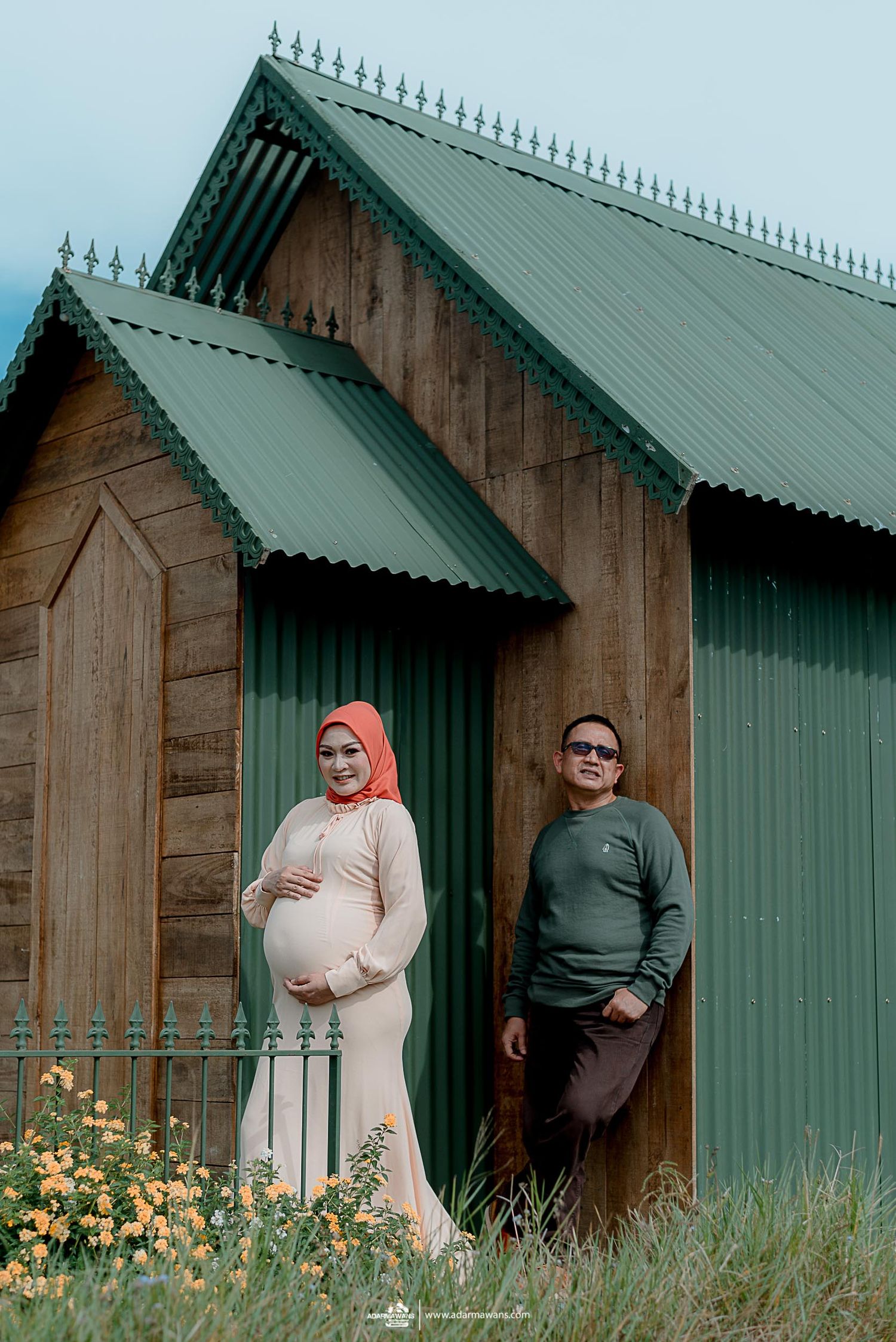 Maternity photo at a rustic wooden chapel with green roof and yellow flowers.