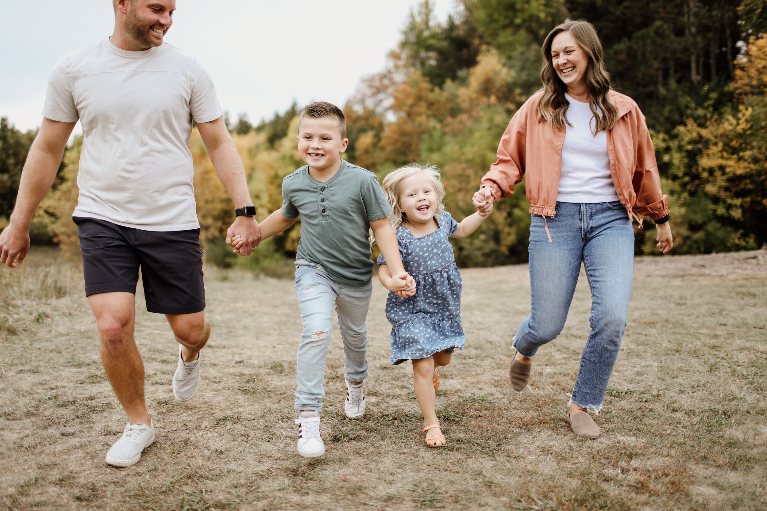 Family holding hands while running together in field during autumn.