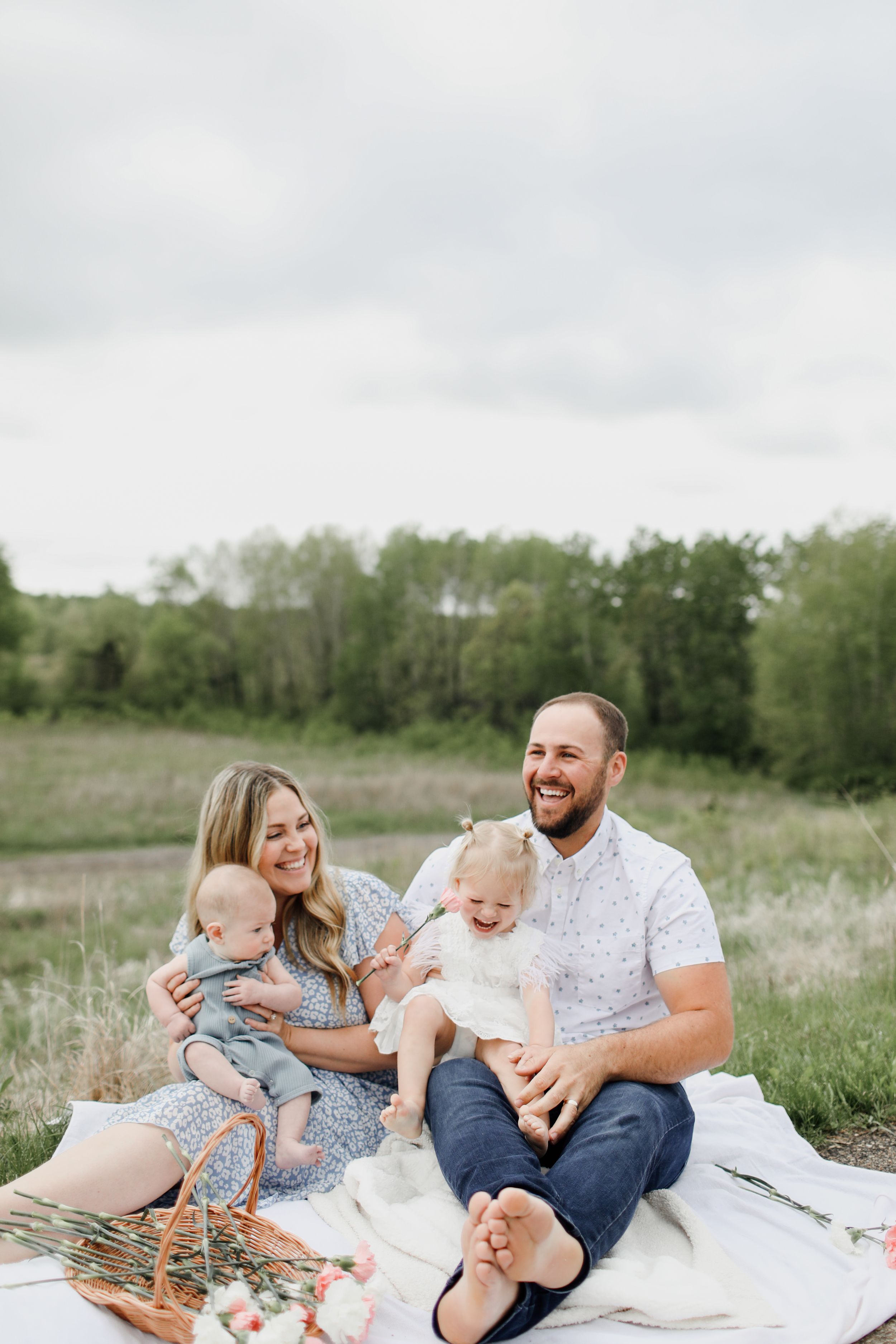 Family enjoying a picnic on a white blanket in a sunny spring meadow.