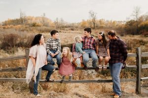 People sitting and posing casually on a wooden fence in an autumn outdoor setting.