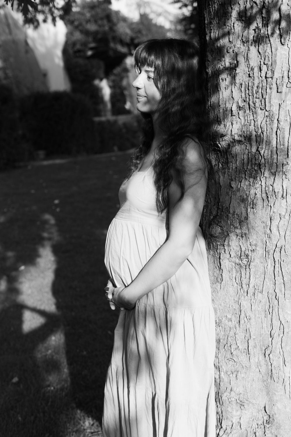 A pregnant woman is leaning against the tree.