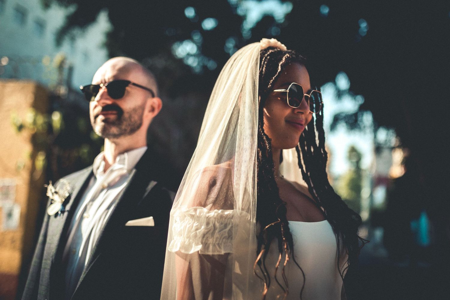 Side profile of wedding couple in sunglasses against urban backdrop.