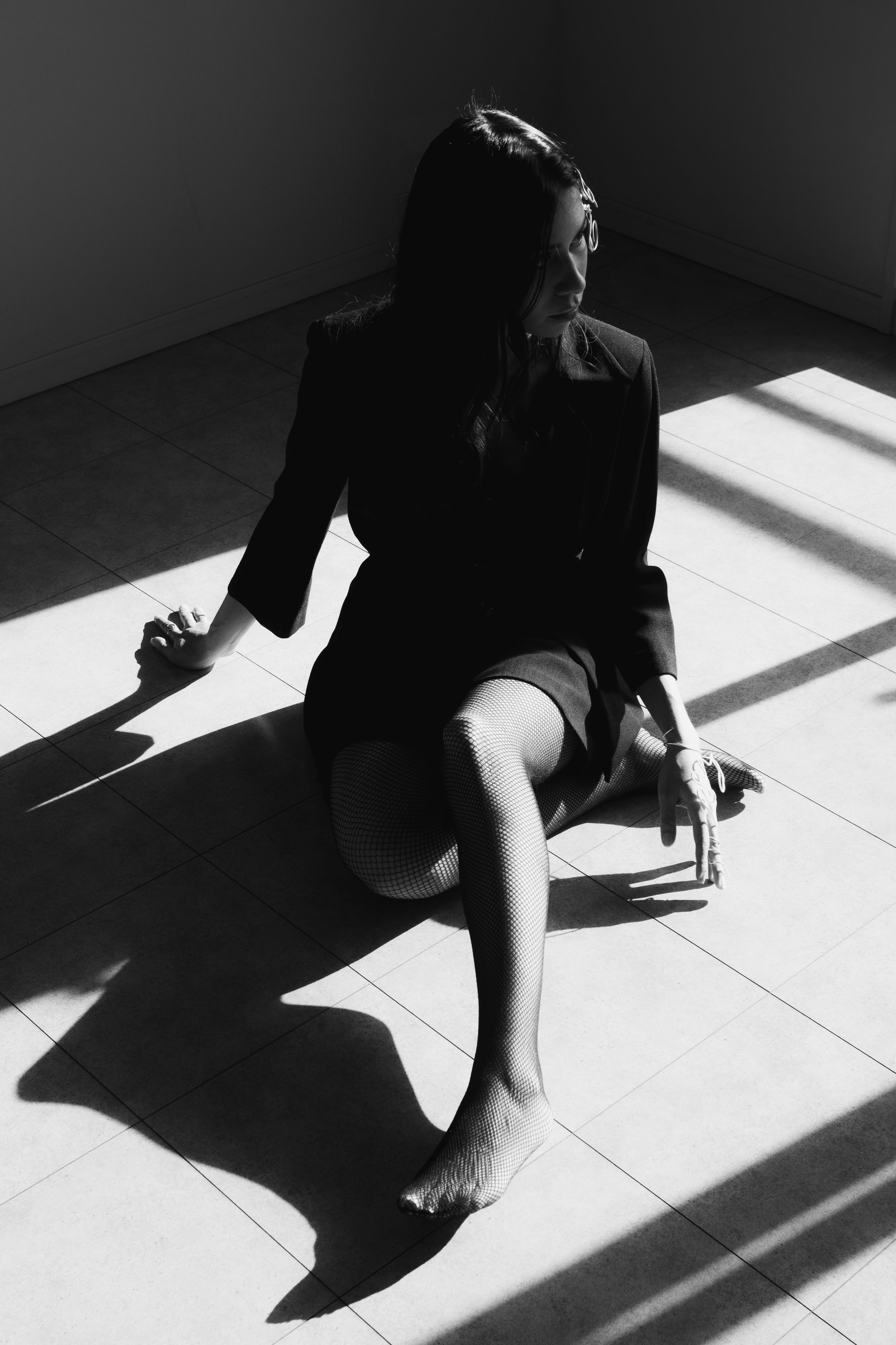 High contrast black and white photo of figure sitting in geometric window light.