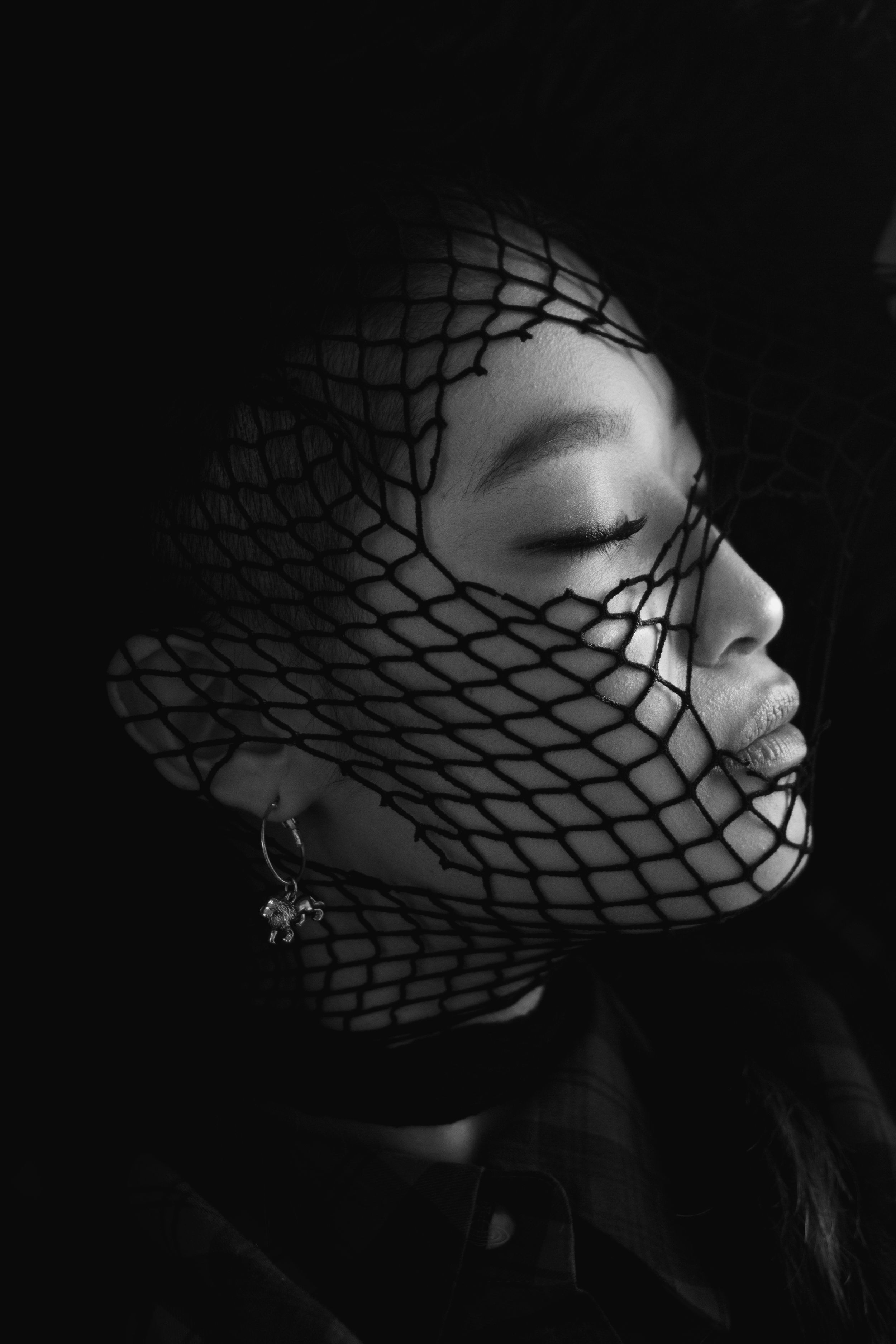 Artistic black and white portrait with dramatic mesh shadow pattern across face.