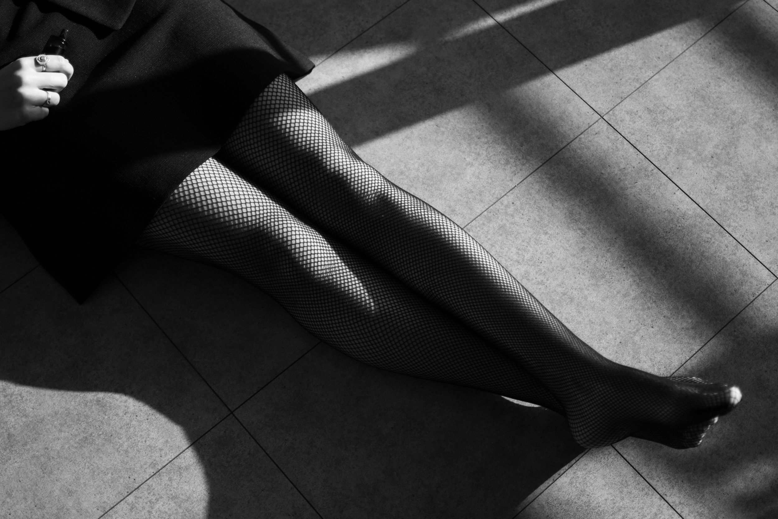 Dramatic black and white photograph of legs in fishnet stockings with strong shadows.