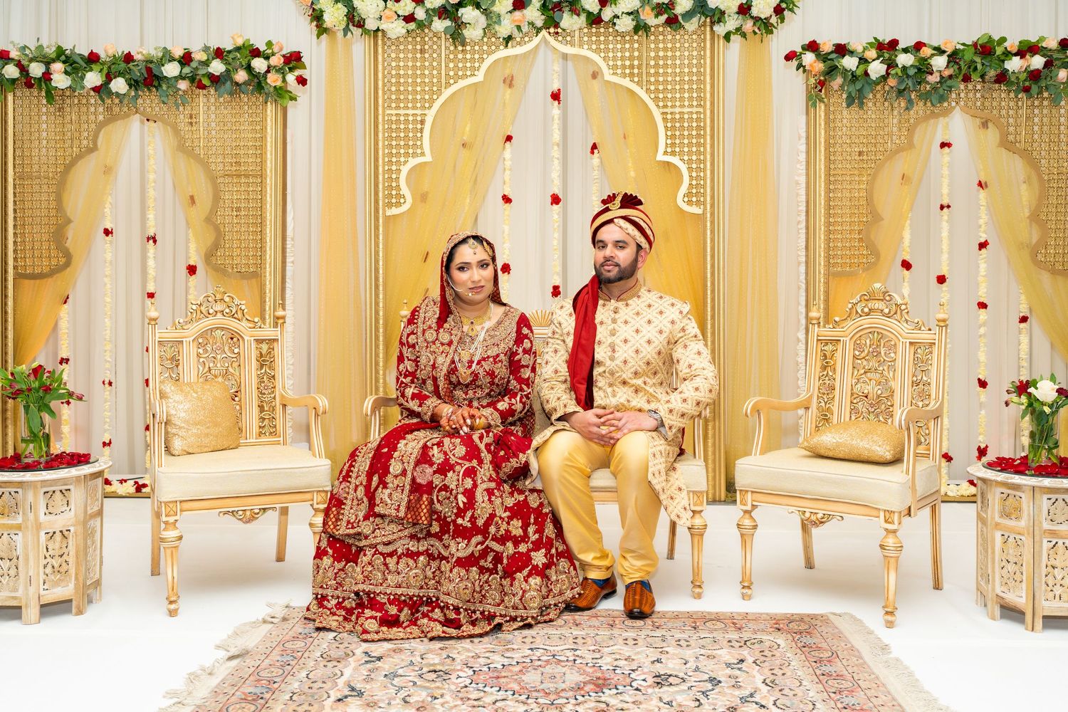 Wedding couple sharing a joyful moment on decorated stage with floral arch and golden chairs.