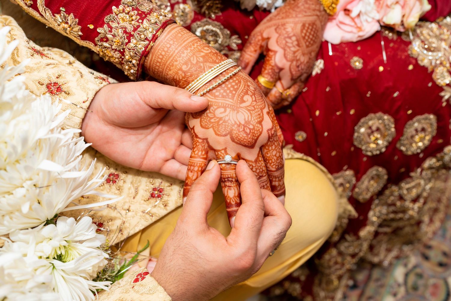 Close-up of hands exchanging rings during traditional South Asian wedding ceremony.