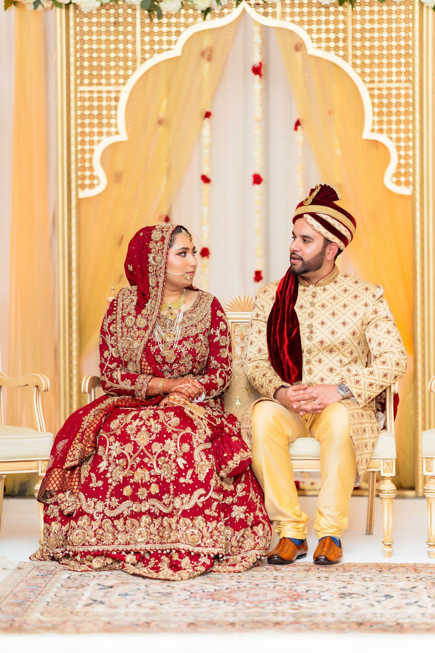 Wedding couple in traditional Indian attire seated on ornate gold chairs during ceremony.