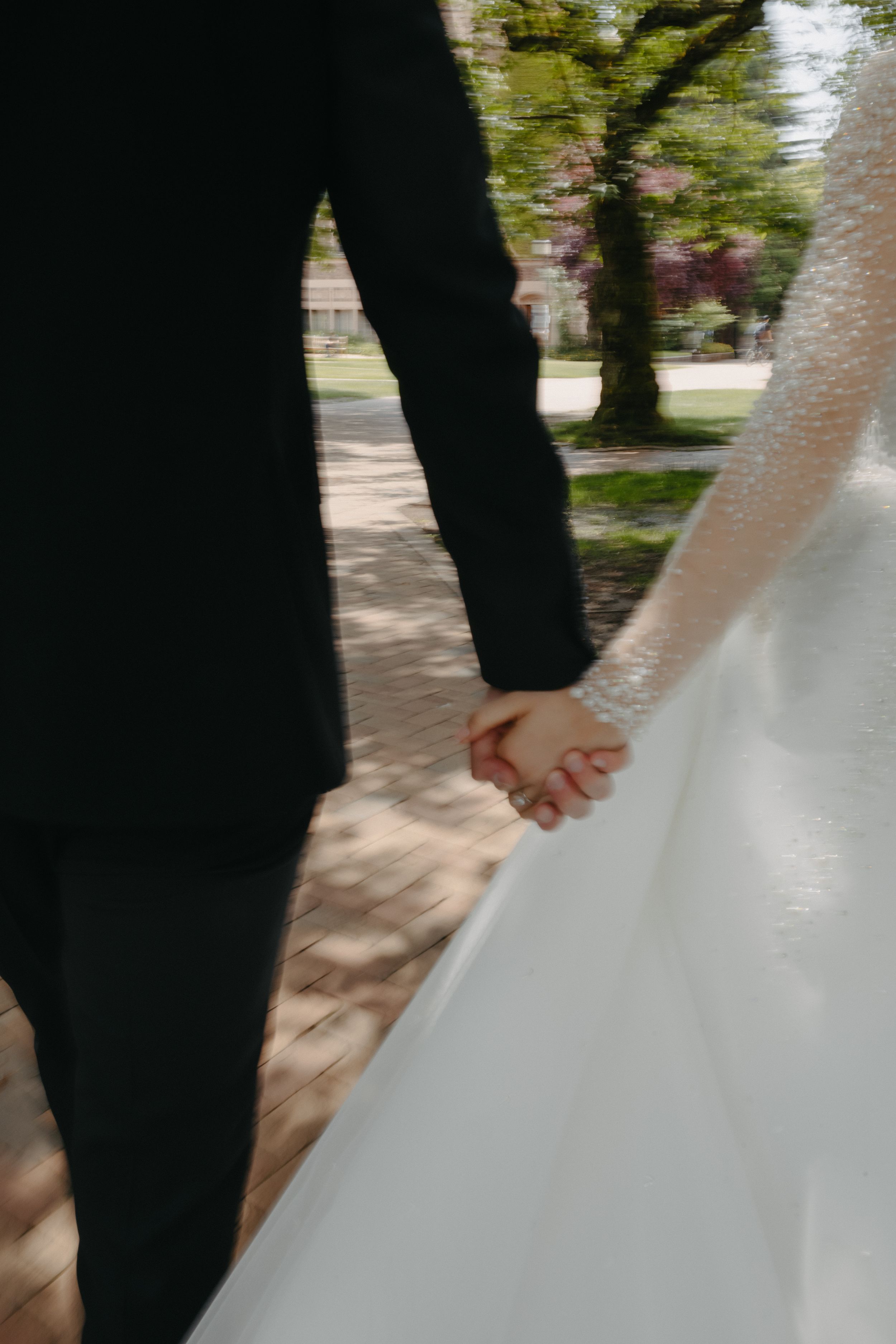 A close-up shot of a couple holding hands on their wedding day against a blurred outdoor background.