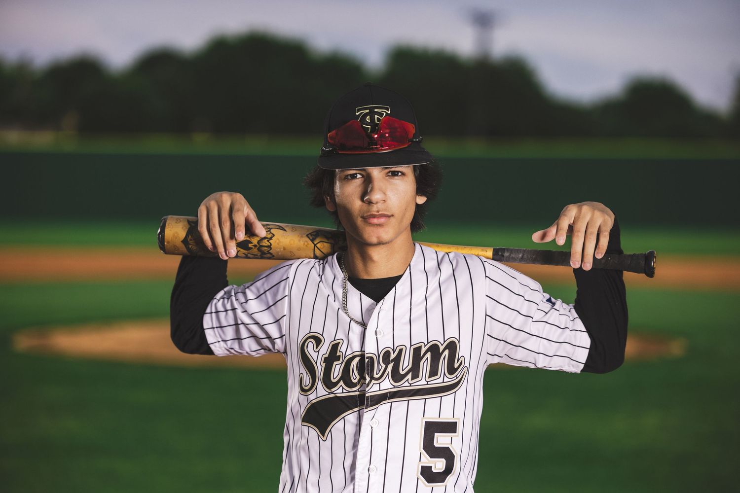Baseball player in pinstripe uniform holding bat across shoulders on field.